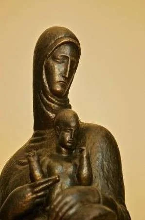 Bronze sculpture of the Virgin Mary in a hood, holding the infant Jesus, with downcast eyes
